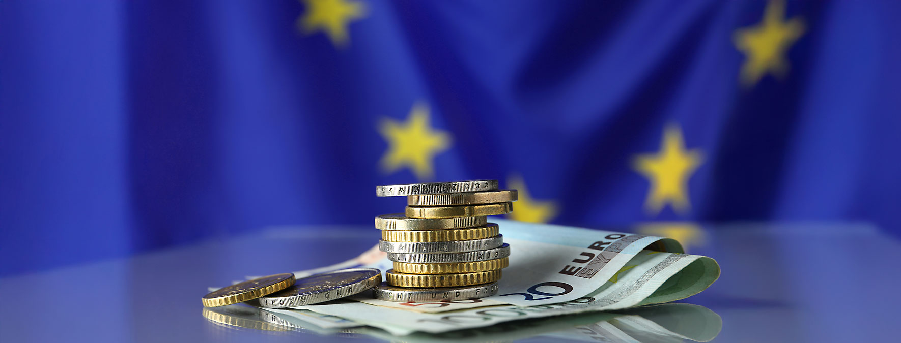 In the foreground coins and bills in the background the European flag